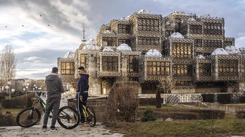 Zwei junge Männer stehen mit ihren Fahrrädern vor der Nationalbibliothek des Kosovo in Pristina.