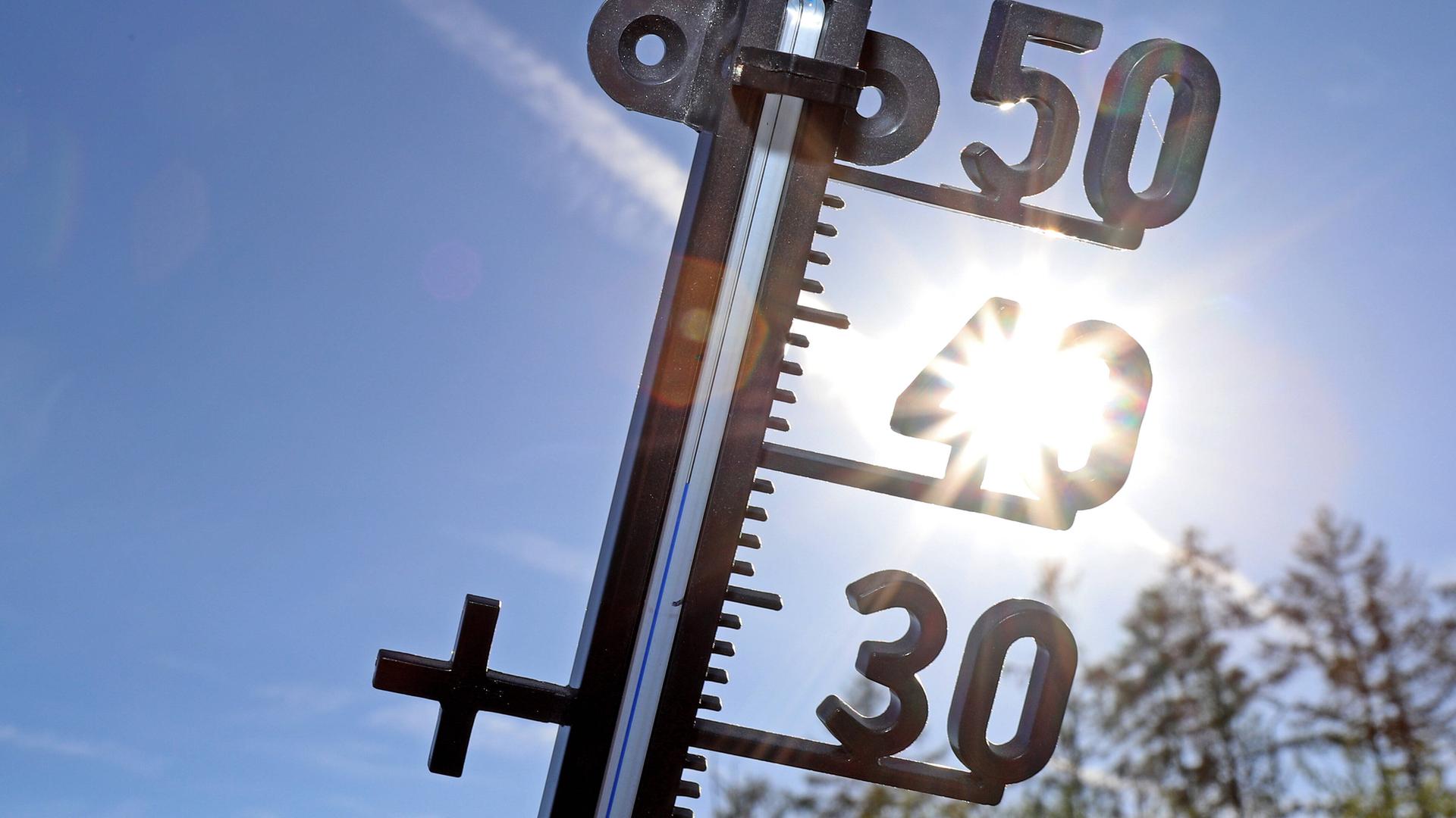 Ein Thermometer vor blauem Himmel und der Sonne 