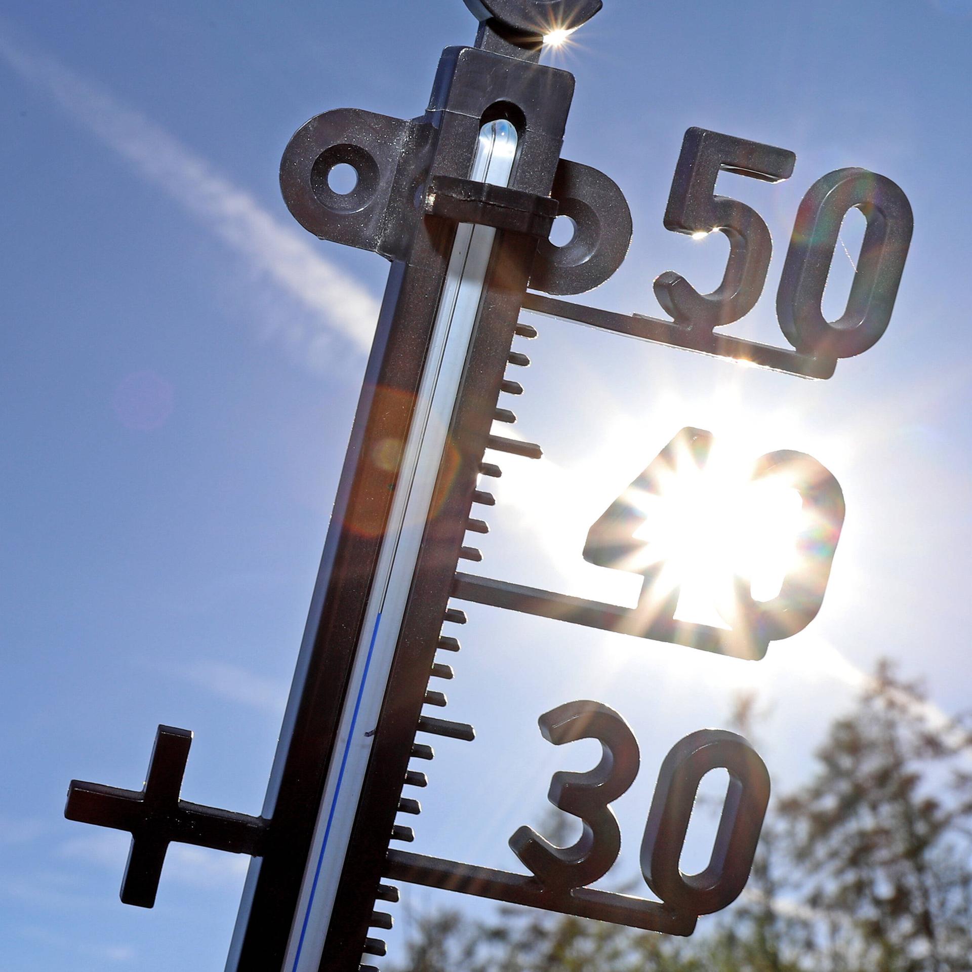 Ein Thermometer vor blauem Himmel und der Sonne 