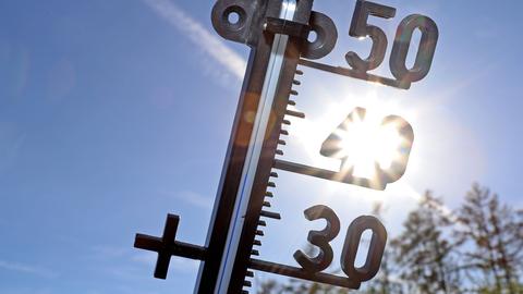 Ein Thermometer vor blauem Himmel und der Sonne 