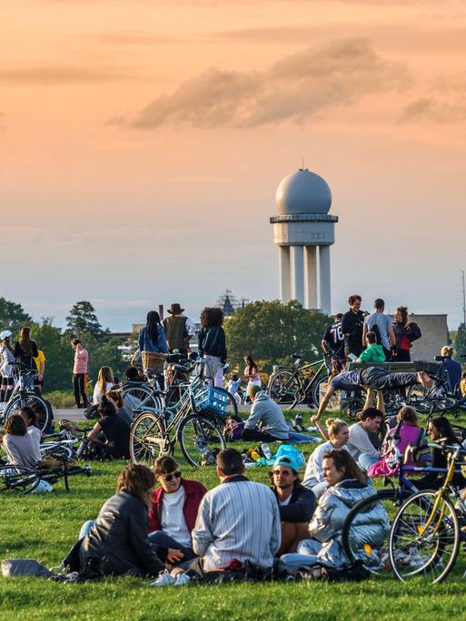 Berlin: Junge Menschen stehen und sitzen auf einer Rasenfläche.