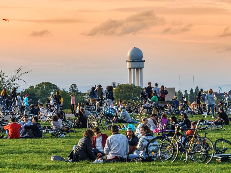 Berlin: Junge Menschen stehen und sitzen auf einer Rasenfläche.