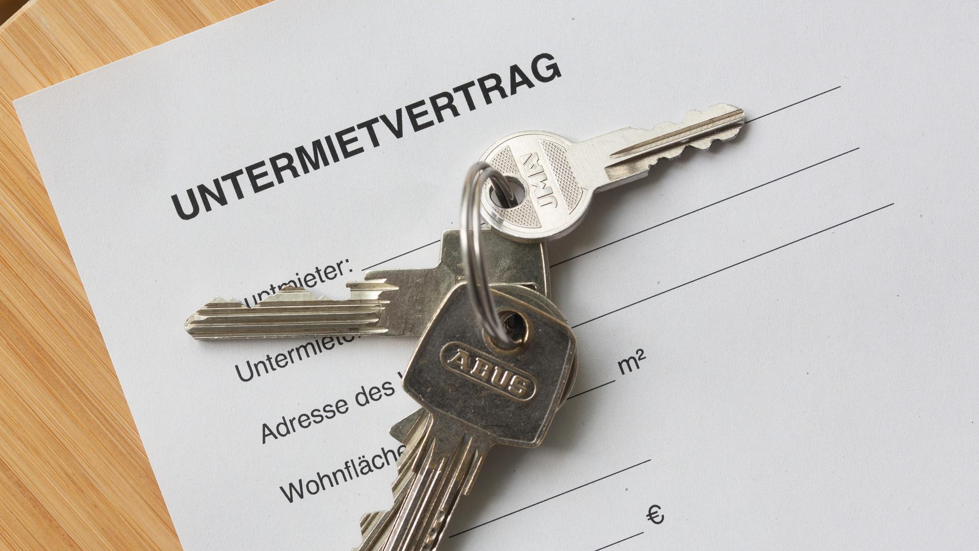 Ein Untermietvertrag liegt zusammen mit Wohnungsschlüsseln auf einem Tisch. Ein Untermietvertrag liegt zusammen mit Wohnungsschlüsseln auf einem Tisch.