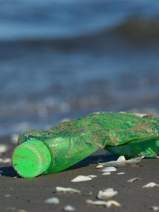 Nahaufnahme einer angespülten grünen Plastikflasch an einem Strand.