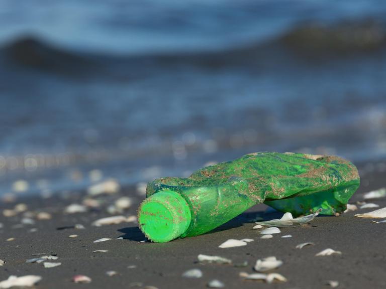 Nahaufnahme einer angespülten grünen Plastikflasch an einem Strand.