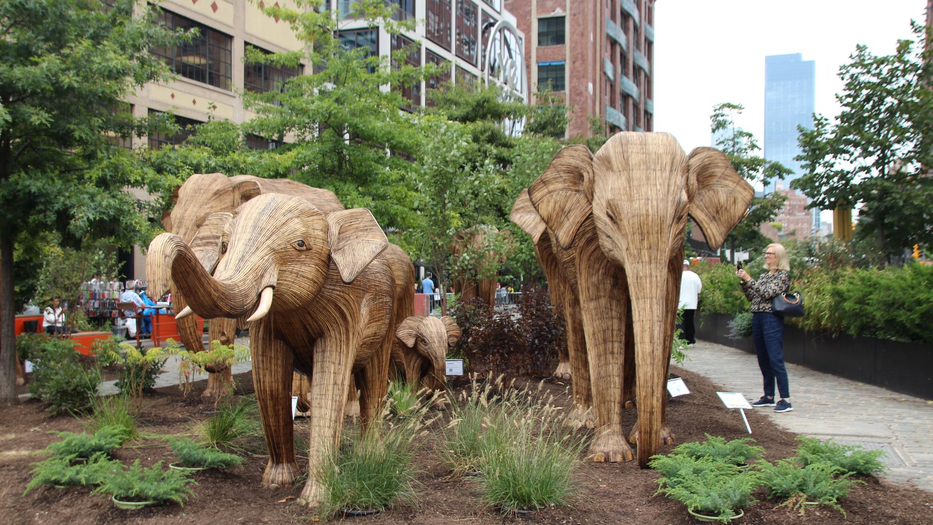 Lebensgroße Elefanten-Statuen aus Holz vor Häusern in New York. Touristen machen Fotos davon.