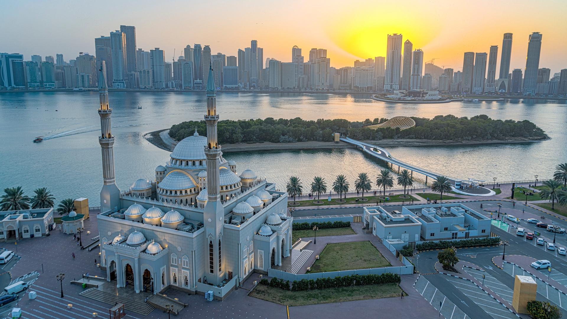 Blick auf eine vorgelagerte Insel mit Hochhäusern, im Vordergrund eine Moschee, hinten der Sonnenuntergang. 