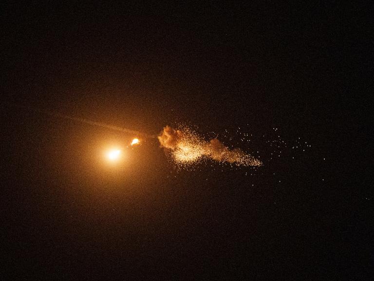 Im Nachthimmel explodiert etwas. Trümmerteile schweben wolkenartig in der Luft. Beleuchtet wird der Moment nur durch die Explosion selbst.