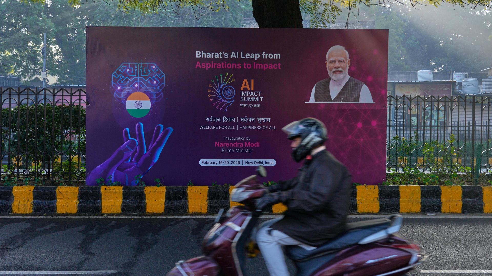 Neu Delhi: Ein Rollerfahrer fährt an einem Banner des KI-Gipfels mit dem indischen Premierminister Narendra Modi vorbei, das auf einer Straße zum Veranstaltungsort des Gipfels steht. Neu Delhi: Ein Rollerfahrer fährt an einem Banner des KI-Gipfels mit dem indischen Premierminister Narendra Modi vorbei, das auf einer Straße zum Veranstaltungsort des Gipfels steht.