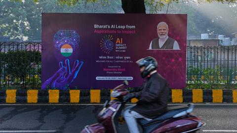 Neu Delhi: Ein Rollerfahrer fährt an einem Banner des KI-Gipfels mit dem indischen Premierminister Narendra Modi vorbei, das auf einer Straße zum Veranstaltungsort des Gipfels steht.