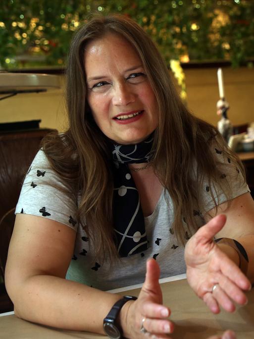 Die Autorin Tanja Dückers. Sie hat lange braune Haare, trägt ein T-Shirt und sitzt draußen an einem Tisch.