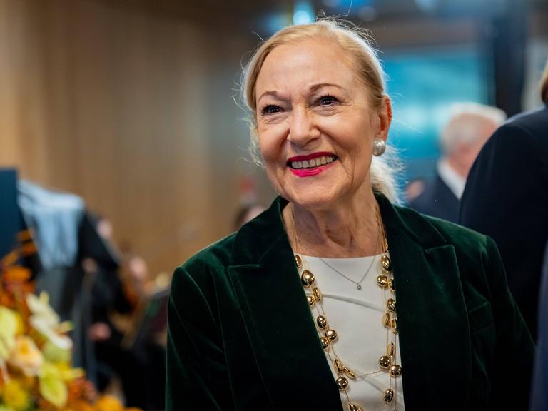 Benita Ferrero-Waldner lächelt in festlicher Kleidung ihr Gegenüber im Off an.