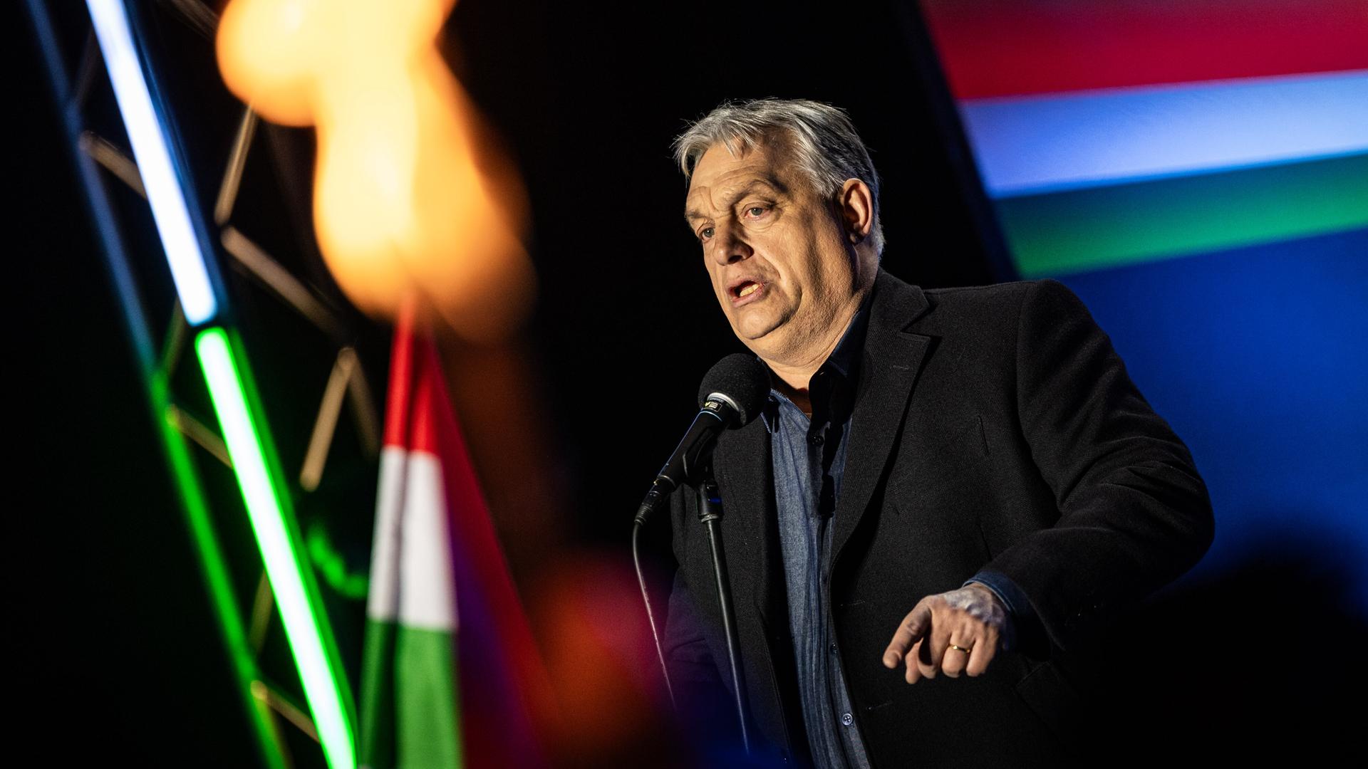 Viktor Orbán steht bei einer Veranstaltung zwischen ungarischen Flaggen auf der Bühne und spricht zu seinem Publikum.