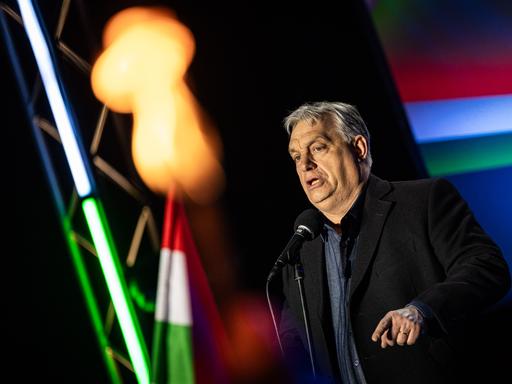 Viktor Orbán steht bei einer Veranstaltung zwischen ungarischen Flaggen auf der Bühne und spricht zu seinem Publikum.