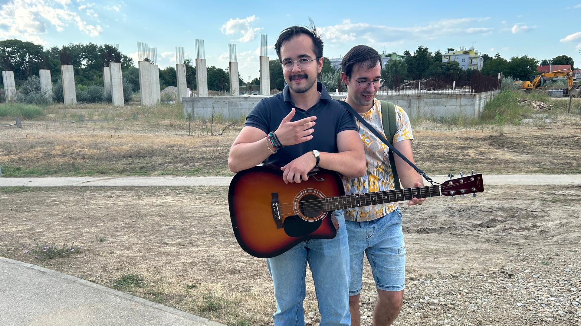 Zwei Männer, einer mit Gitarre, stehen vor einer Bauruine im kroatischen Vukovar