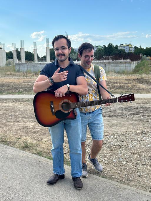 Zwei Männer, einer mit Gitarre, stehen vor einer Bauruine im kroatischen Vukovar Zwei Männer, einer mit Gitarre, stehen vor einer Bauruine im kroatischen Vukovar