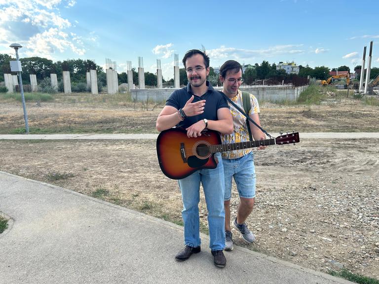 Zwei Männer, einer mit Gitarre, stehen vor einer Bauruine im kroatischen Vukovar Zwei Männer, einer mit Gitarre, stehen vor einer Bauruine im kroatischen Vukovar
