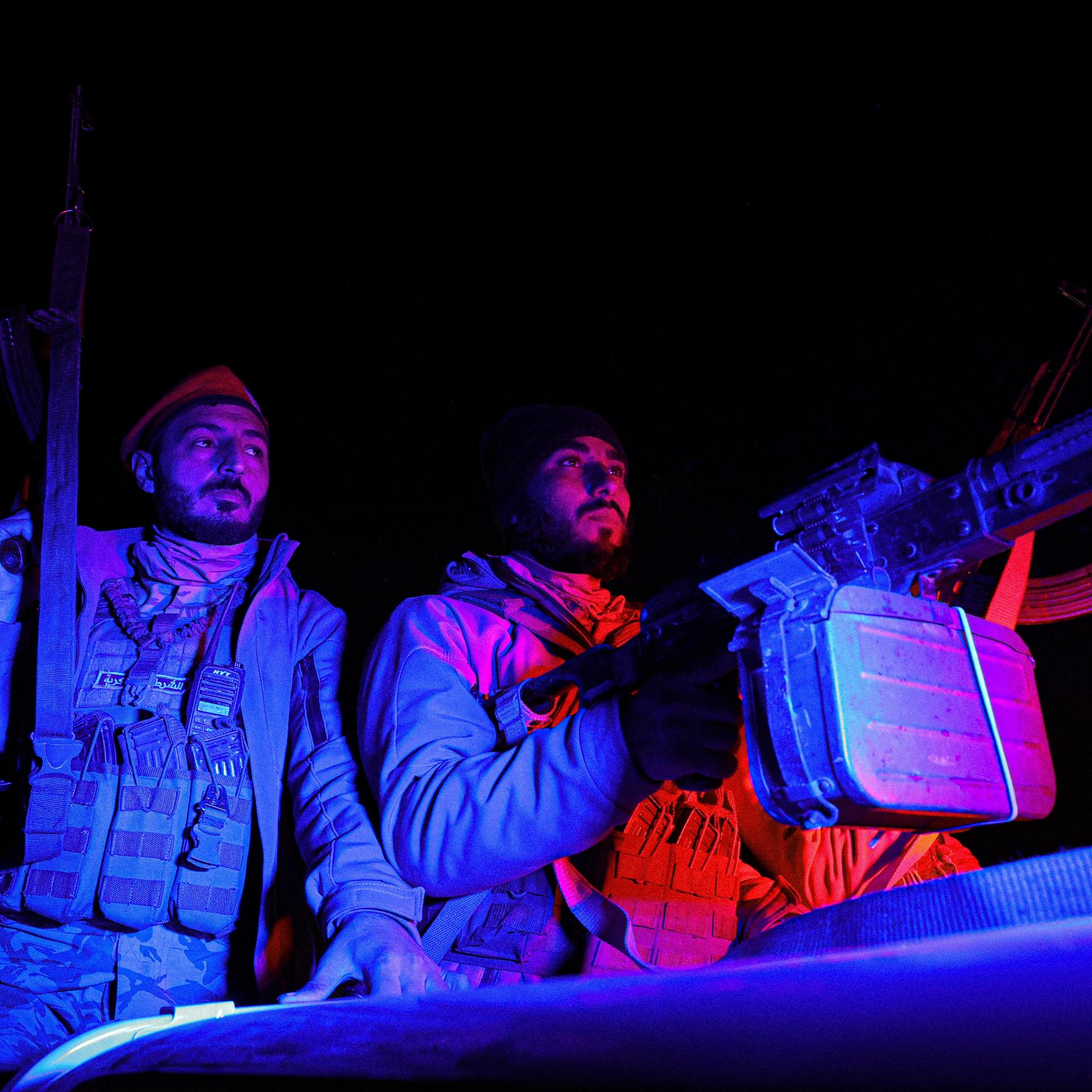 Es ist dunkel. Die beiden Soldaten sitzen auf einem Fahrzeug mit Haubitze. Sie werden bläulich angestahlt. 