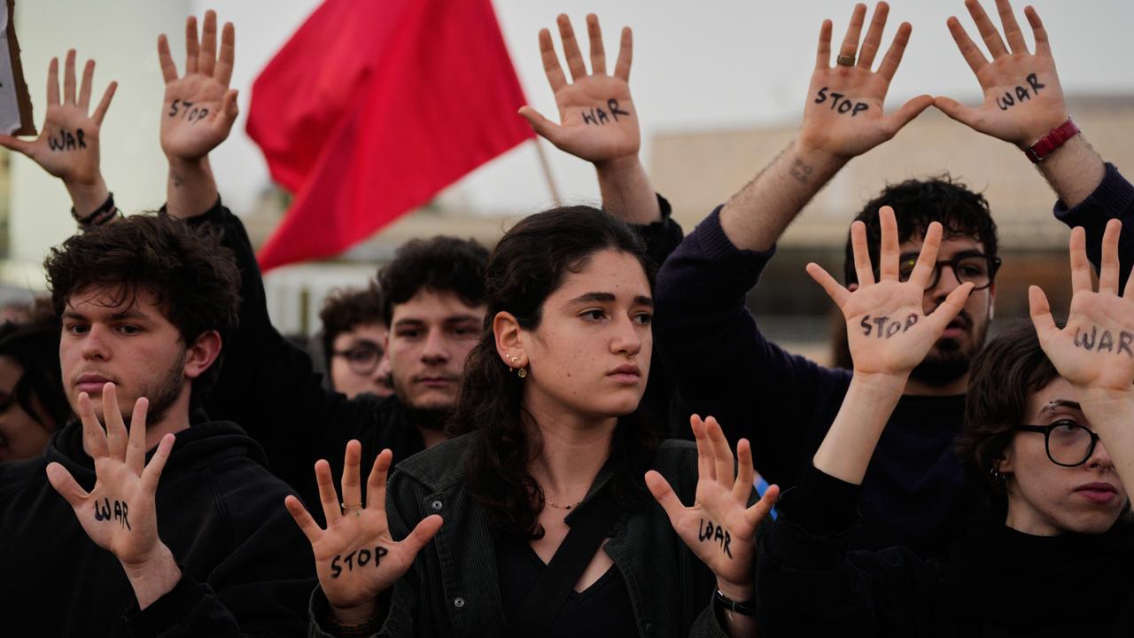 Mehrere Menschen stehen nebeneinander. Sie sind schwarz gekleidet. Auf ihren Handflächen steht in schwarzer Farbe "Stop" und "War". 