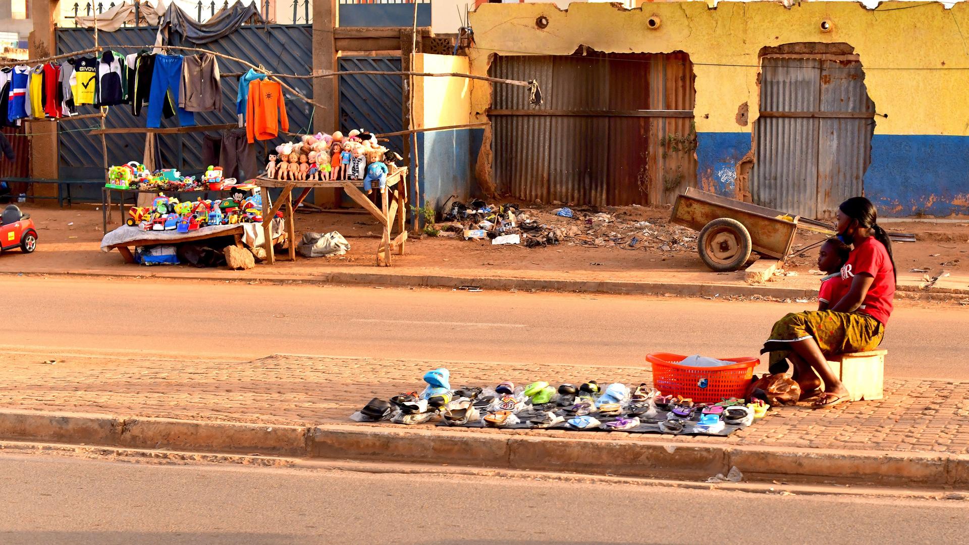 Eine burkinische Frau sitzt mit ihrem Kind auf dem Mittelstreifen einer Straße in der Hauptstadt Ouagadougou und versucht, von ihrem mobilen Verkaufsstand aus, Vorbeifahrenden ihre Waren zu verkaufen.