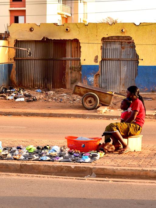 Eine burkinische Frau sitzt mit ihrem Kind auf dem Mittelstreifen einer Straße in der Hauptstadt Ouagadougou und versucht, von ihrem mobilen Verkaufsstand aus, Vorbeifahrenden ihre Waren zu verkaufen.