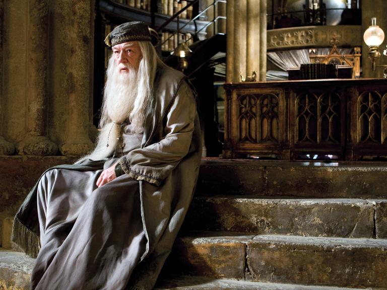 Michael Gambon sitzt als Dumbledore auf einer Treppe in seinem Büro.