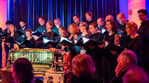Die Sängerinnen und Sänger des Rundfunkchores Berlin stehen versammelt um ein Trautorium und singen.