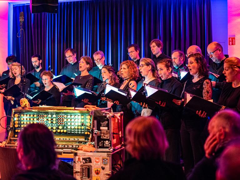 Die Sängerinnen und Sänger des Rundfunkchores Berlin stehen versammelt um ein Trautorium und singen.