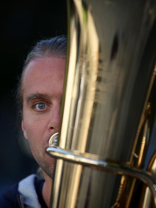 Andreas Martin Hofmeir posiert mit seiner Tuba. Nur eine Hälfte seines Gesichts schaut hinter der Tuba vor.