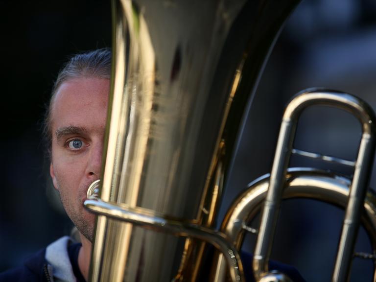 Andreas Martin Hofmeir posiert mit seiner Tuba. Nur eine Hälfte seines Gesichts schaut hinter der Tuba vor.