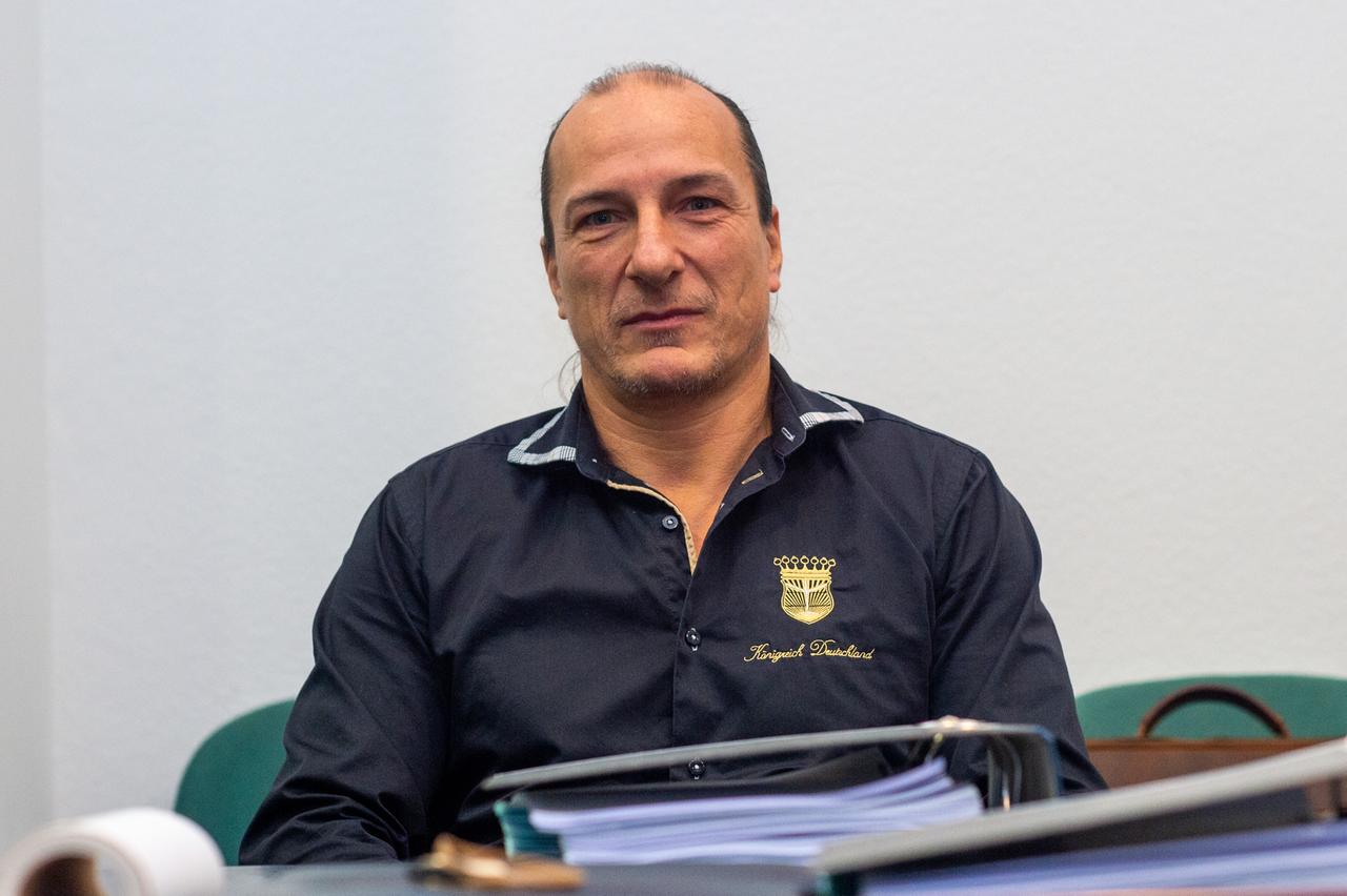Peter Fitzek sitzt in einem Gerichtssaal hinter Aktenordnern und trägt ein blaues Hemd, auf dass "Königreich Deutschland" gestickt ist Peter Fitzek sitzt in einem Gerichtssaal hinter Aktenordnern und trägt ein blaues Hemd, auf dass "Königreich Deutschland" gestickt ist