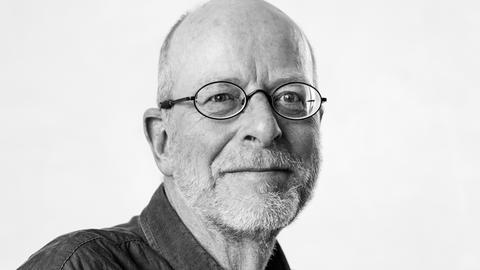 Ein Mann mit Brille und Dreitagebart schaut erfreut in die Kamera