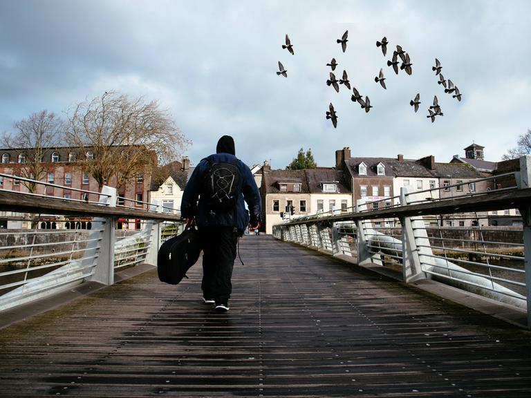 Ein Mann mit einer Gitarre läuft über eine Brücke