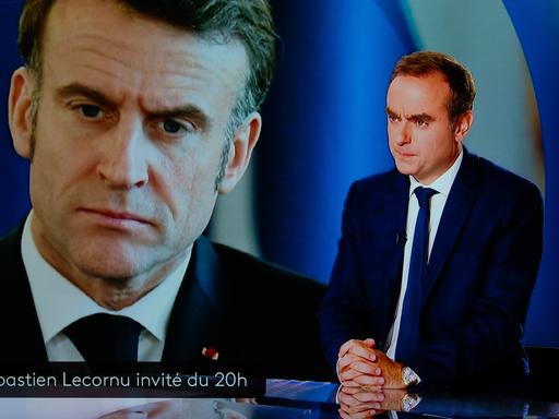 Frankreichs Premier Sebastien Lecornu steht in einem Fernsehstudio, im Hintergrund ist Präsident Macron auf einen Bildschirm projiziert. 