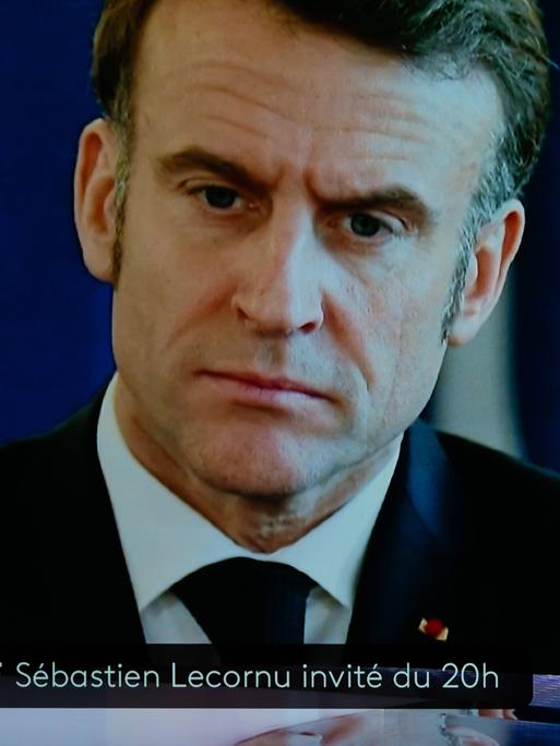 Frankreichs Premier Sebastien Lecornu steht in einem Fernsehstudio, im Hintergrund ist Präsident Macron auf einen Bildschirm projiziert. 