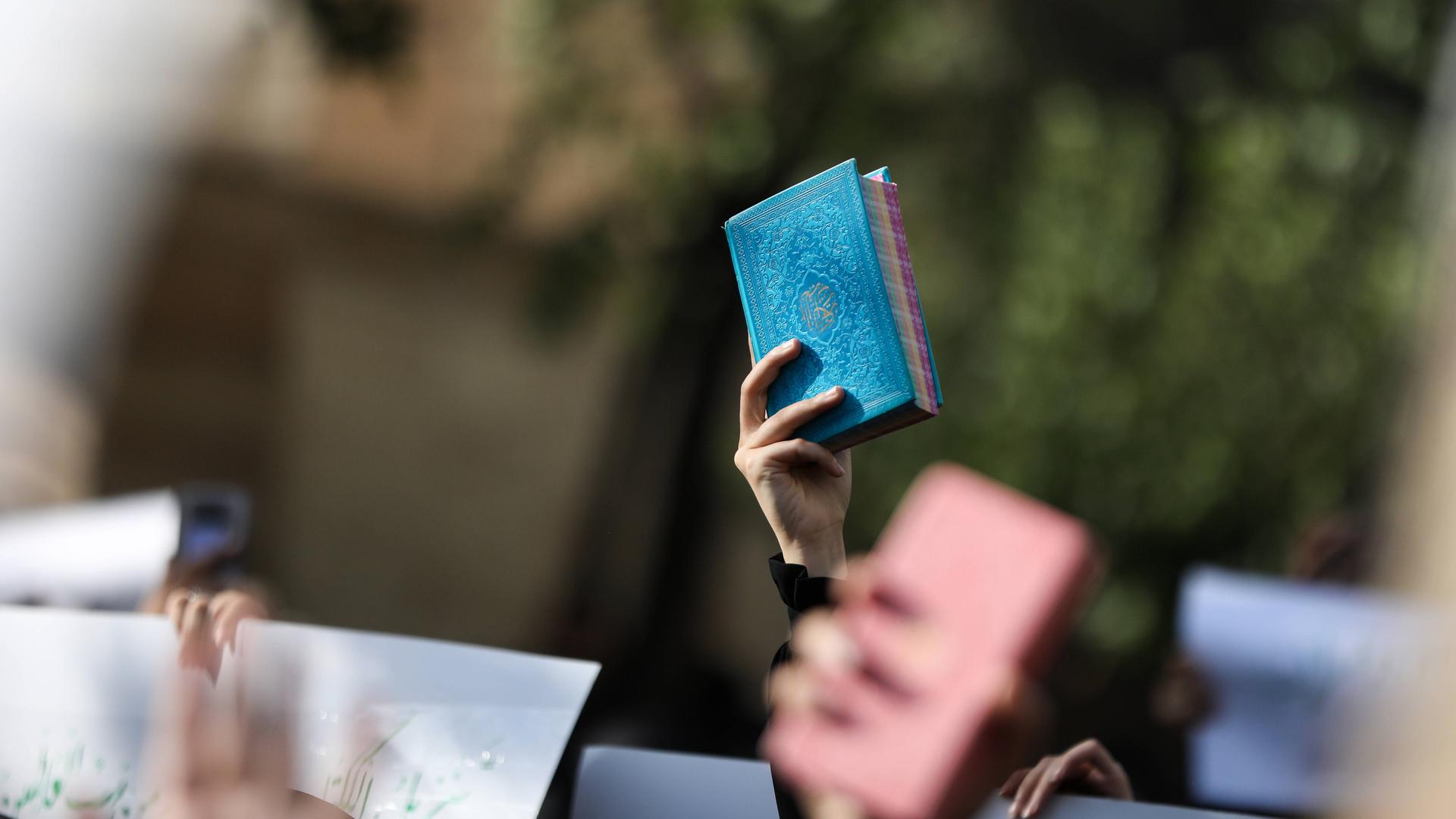Eine hand hält bei einer Demonstration den blau eingebundenen Koran in die Höhe.