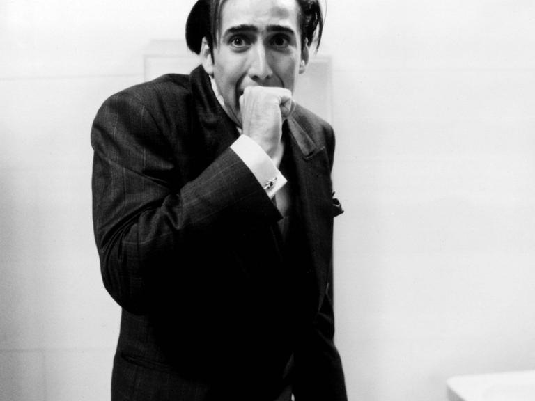 Im Still aus "Vampire's Kiss" beißt Nicolas Cage sich mit gequältem Gesichtsausdruck in die eigene Hand.