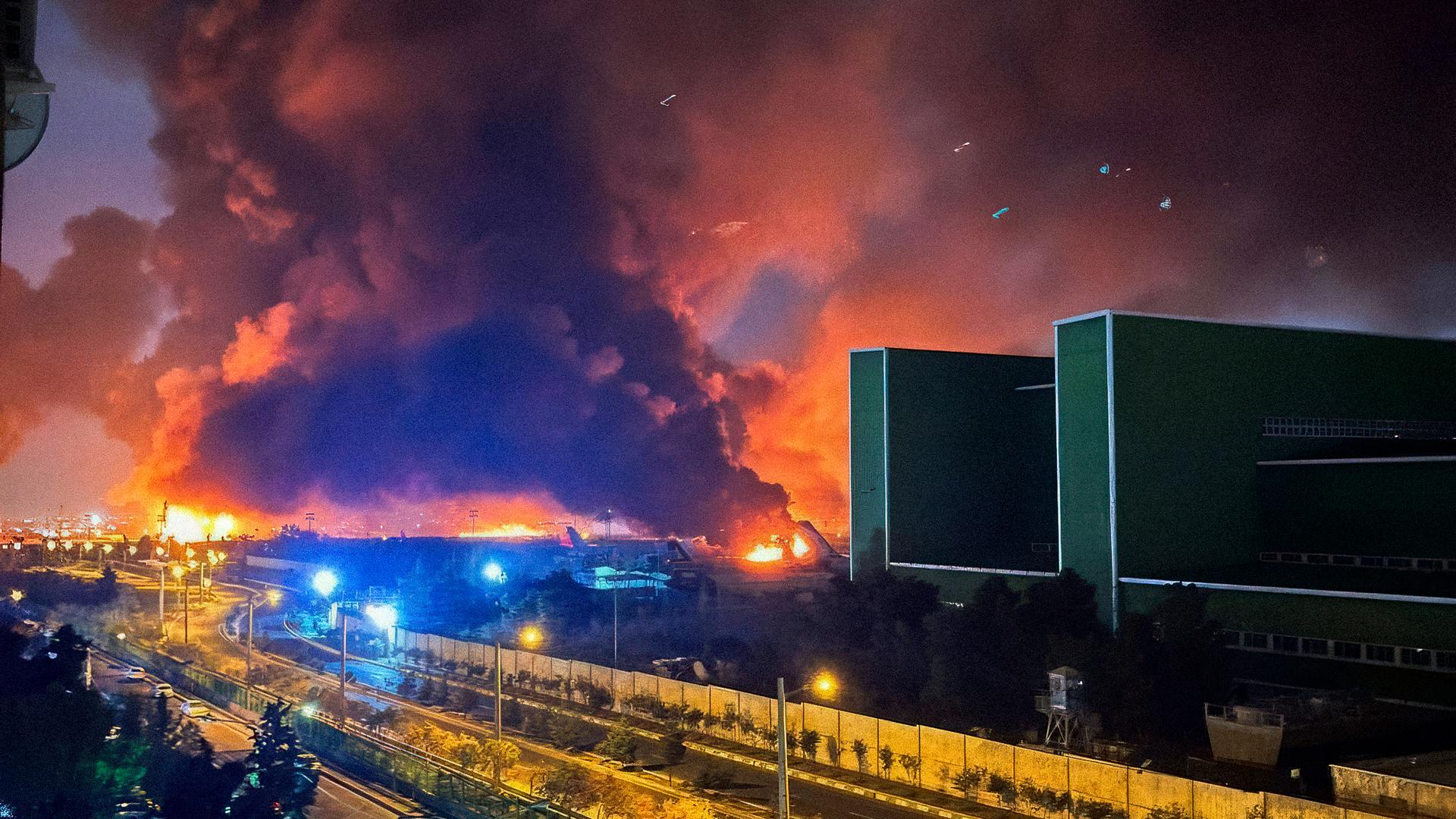Explosionen gab es auch am Internationalen Flughafen in Teheran. Es ist eine riesige Rauchwolke zu sehen; im Vordergrund eine Autobahn und Häuser.