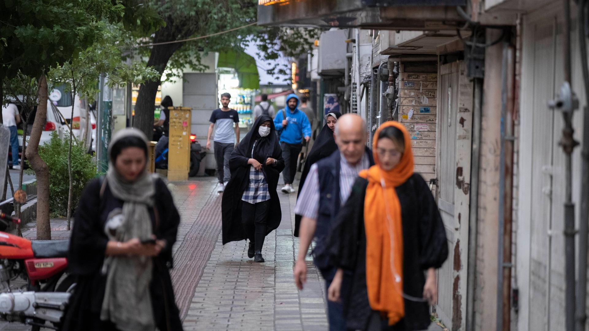 Menschen gehen eine Strase in Teheran herunter. Die Frauen tragen Kopftücher, teilweise auch Corona-Masken.