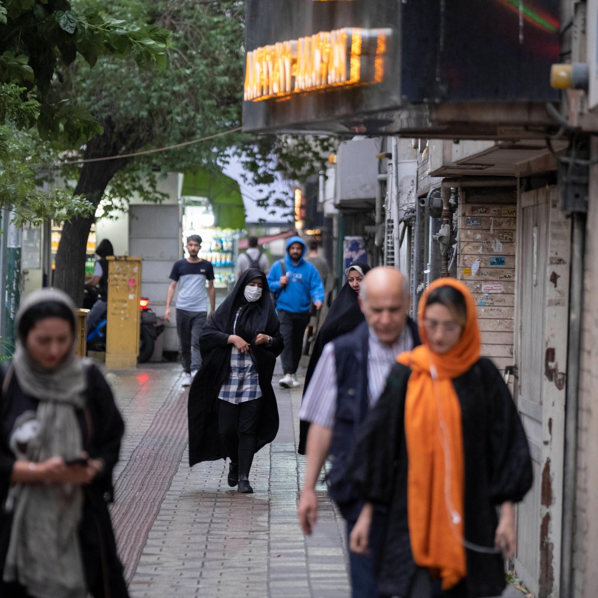Menschen gehen eine Strase in Teheran herunter. Die Frauen tragen Kopftücher, teilweise auch Corona-Masken.