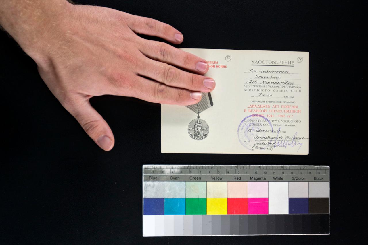Eine Hand arrangiert ein Dokument auf schwarzem Untergrund. Darunter liegt eine Farbkarte.