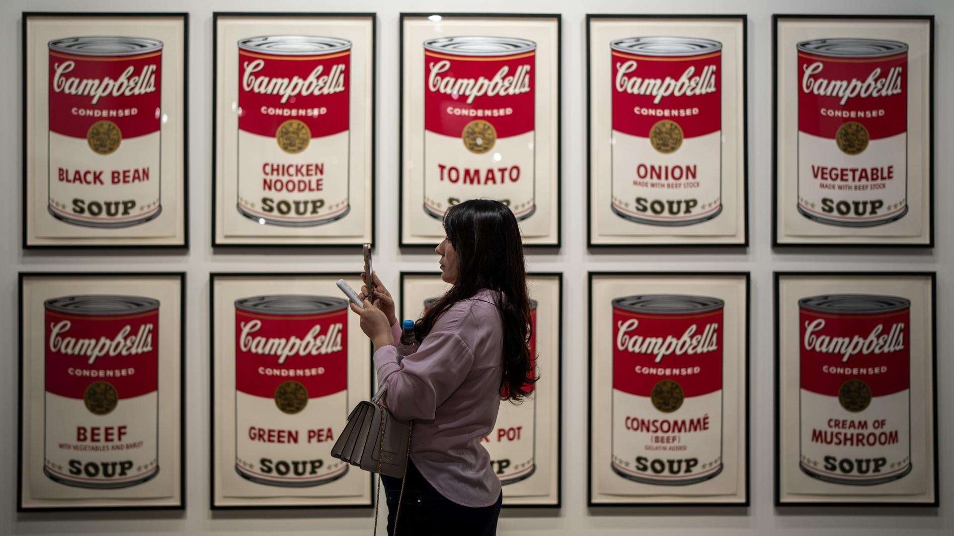 Eine Frau steht vor Bildern mit Suppendosen auf der Art Basel in Hongkong Eine Frau steht vor Bildern mit Suppendosen auf der Art Basel in Hongkong