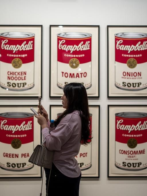 Eine Frau steht vor Bildern mit Suppendosen auf der Art Basel in Hongkong