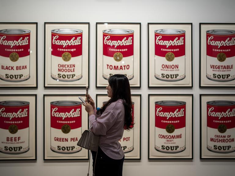 Eine Frau steht vor Bildern mit Suppendosen auf der Art Basel in Hongkong