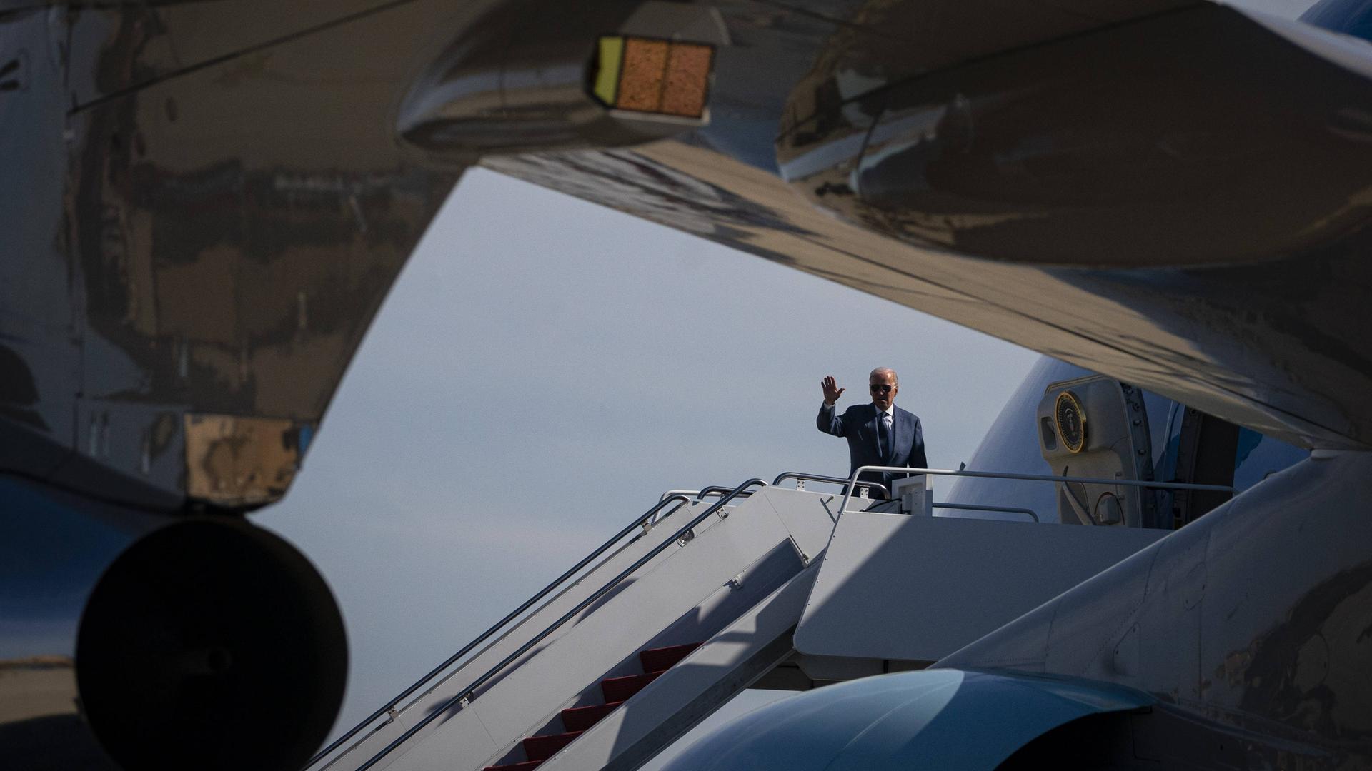 US-Präsident Biden steht auf der Treppe zur Air Force One und winkt. Er trägt einen blauen Anzug. US-Präsident Biden steht auf der Treppe zur Air Force One und winkt. Er trägt einen blauen Anzug.