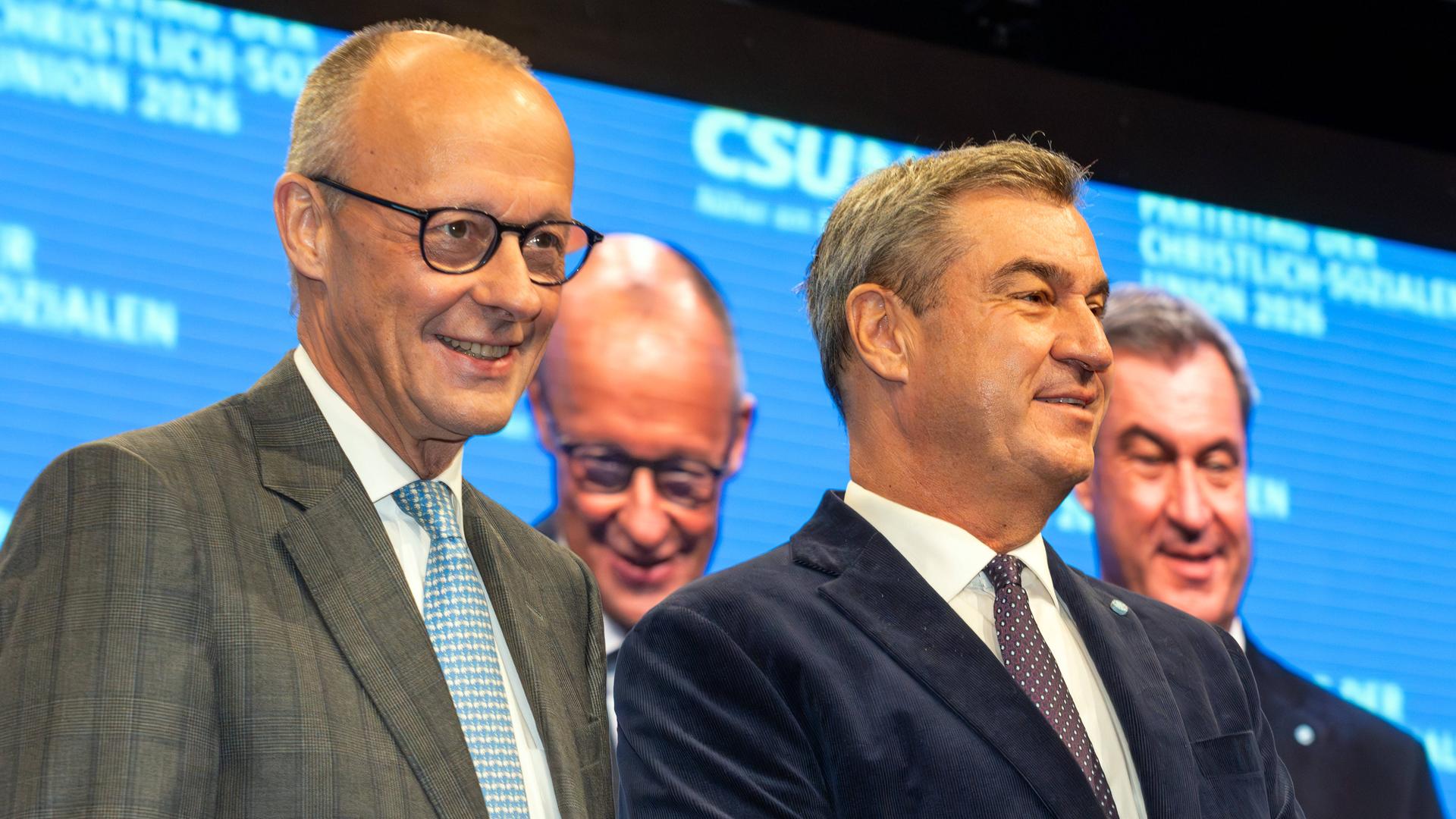Friedrich Merz und Markus Söder auf einer Bühne, dahinter eine Videoleinwand mit ihren Gesichtern.