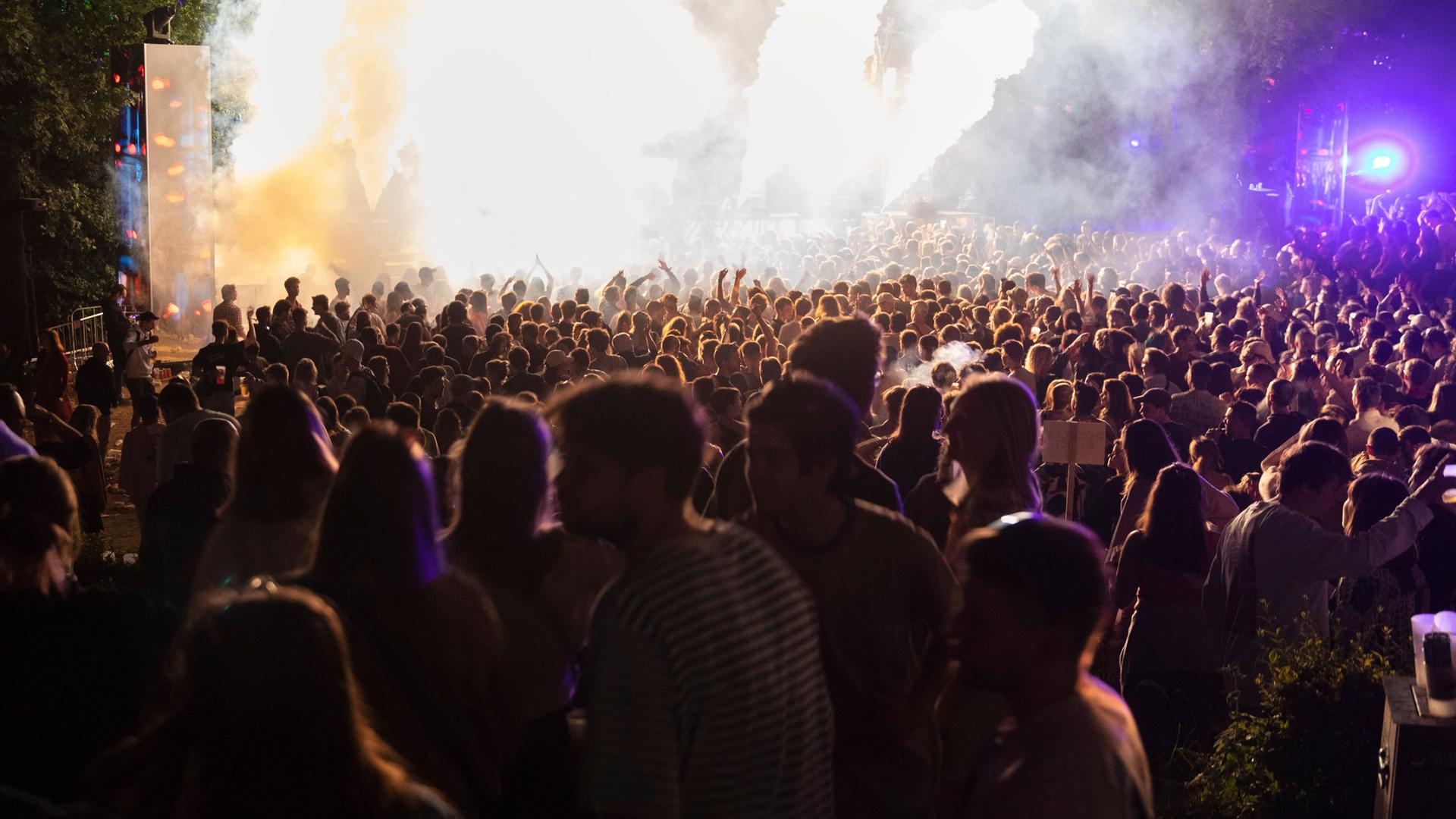 Eine Menge Zuschauer schaut ein Konzert. Auf der Bühne sind Nebelfontänen.