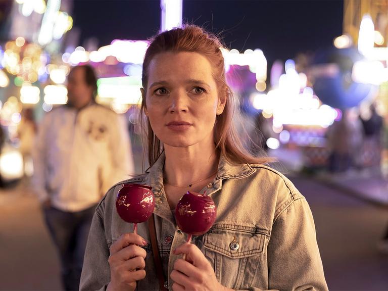 Filmszene aus "Wunderschöner", die Schauspielerin Karoline Herfurth hat rechts und links zwei rote Liebesäpfel in der Hand.