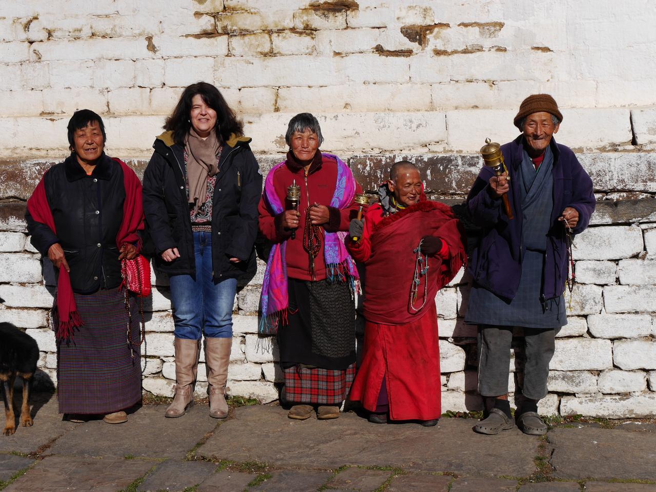 Eine Gruppe lächelnder Bhutanerinnen und Bhutanern in traditioneller Kleidung mit der Reiseagentin Bernita Müller.