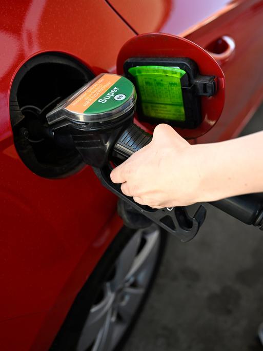 Das Bild zeigt eine Person. Sie betankt ein Auto mit Benzin.